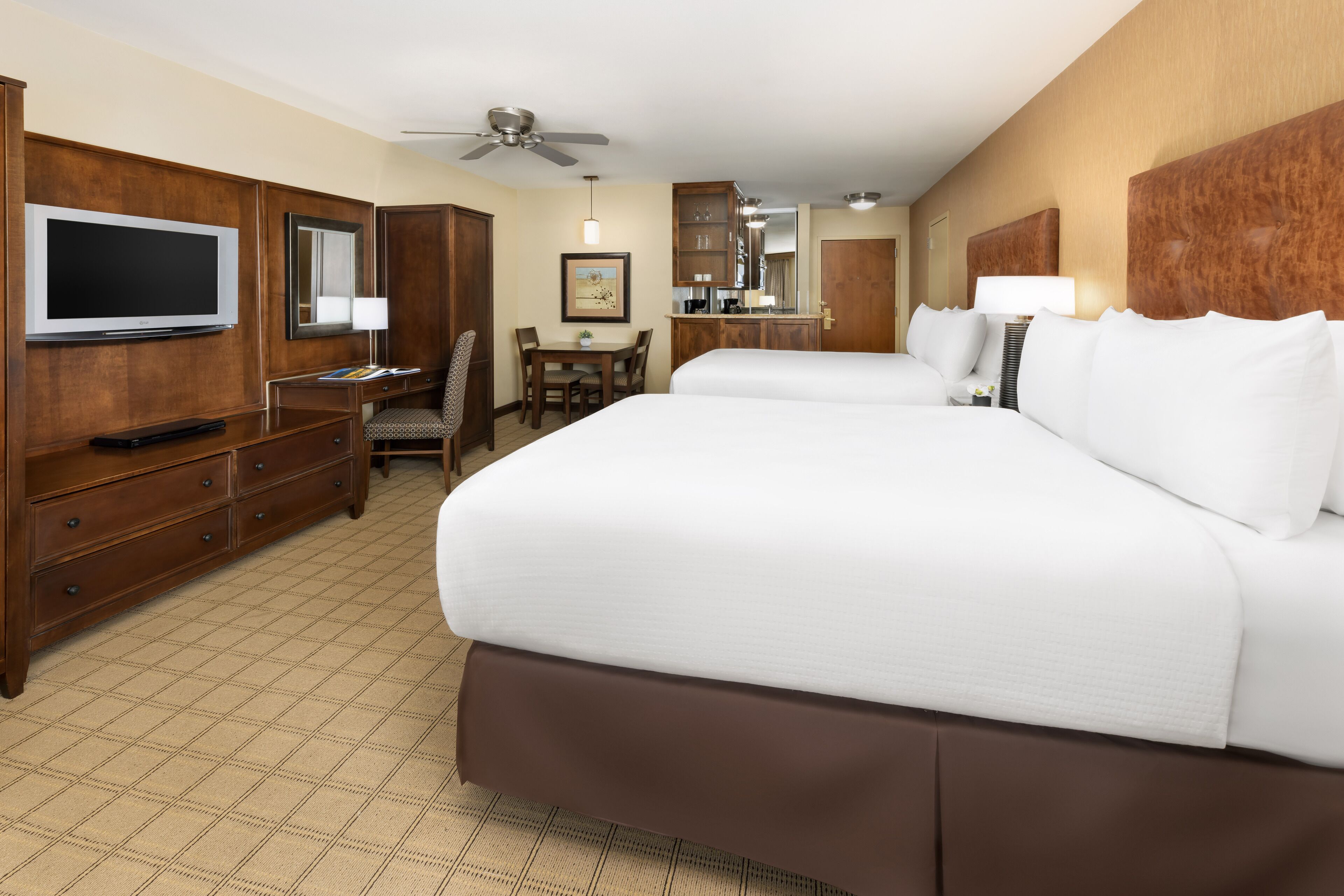 Habitación de hotel con dos camas, televisión, escritorio y zona de comedor.