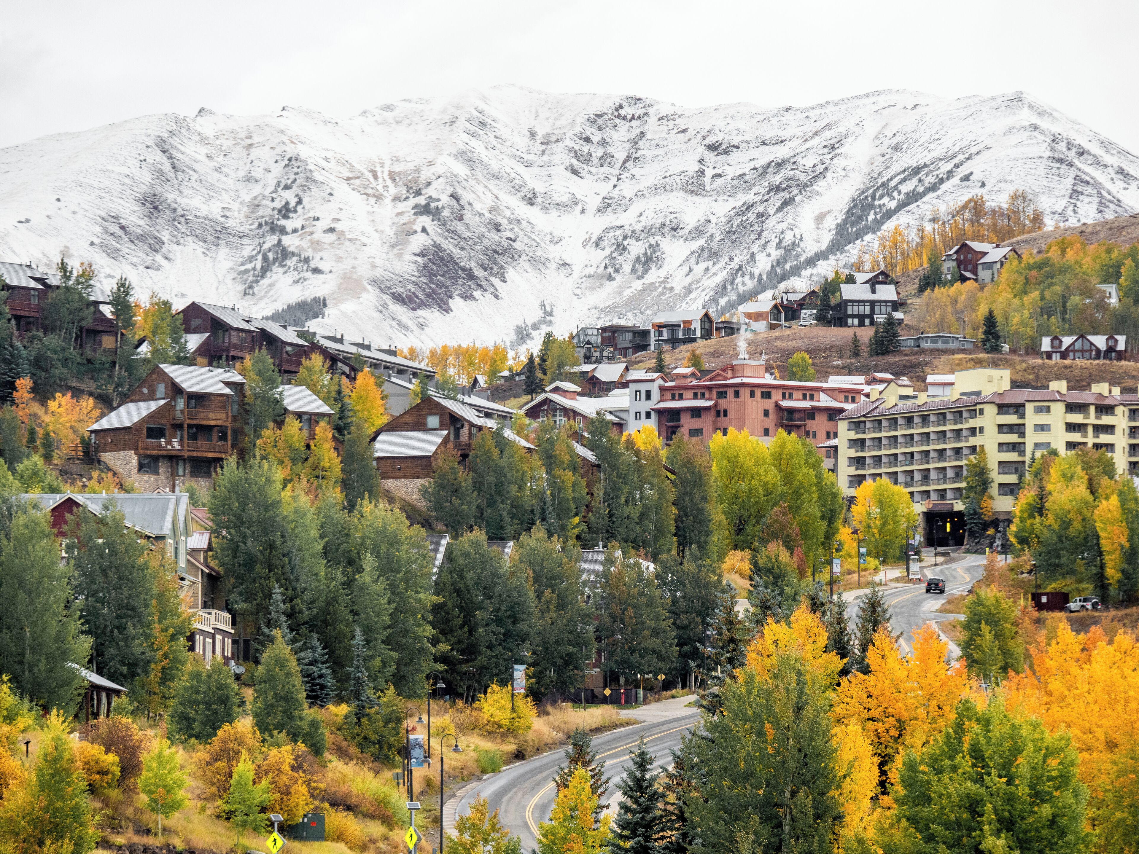 A mountain resort with multi-story buildings, a winding road, and autumn foliage.