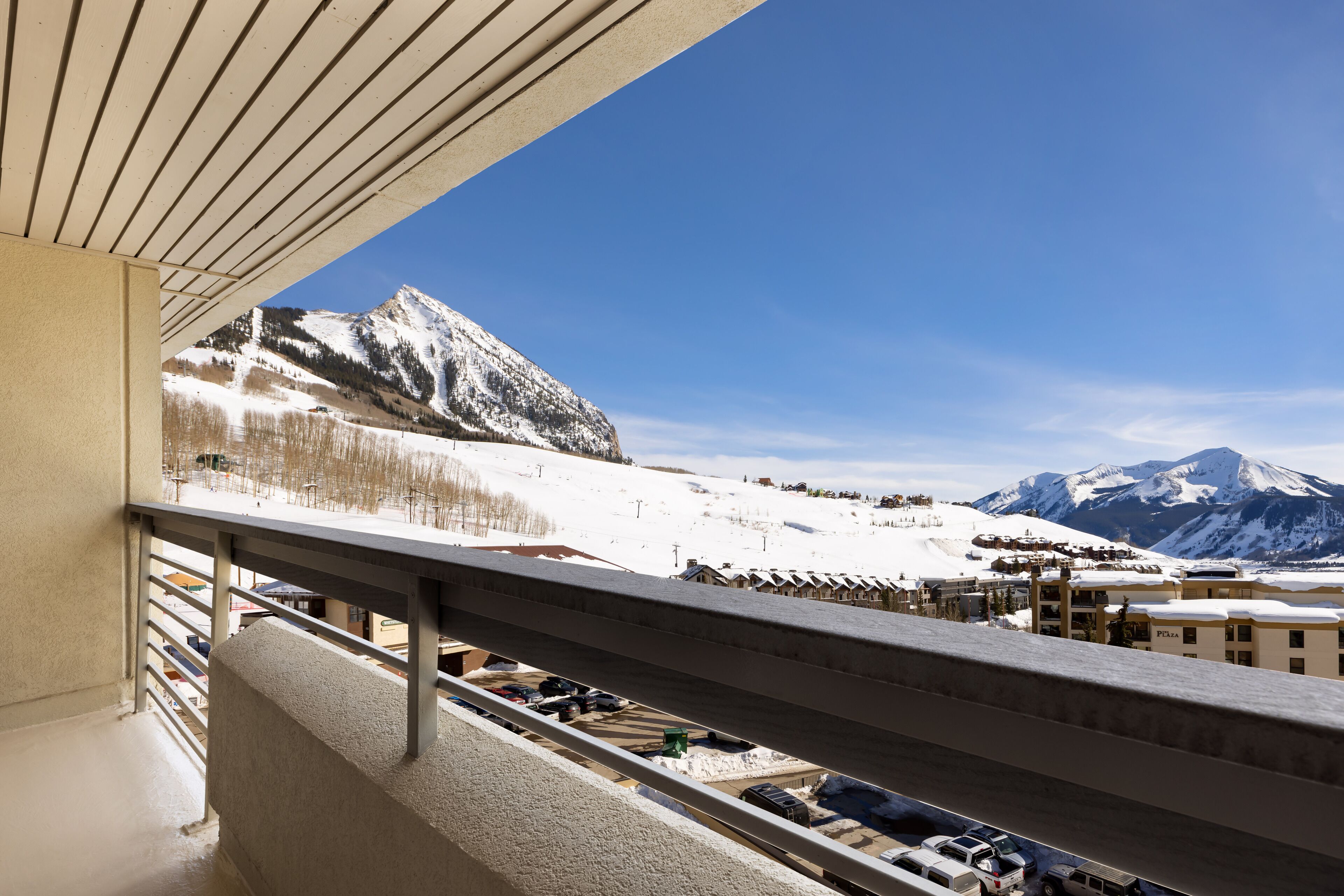 Un balcón con vista a una montaña nevada y un estacionamiento.
