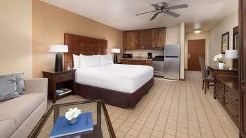 Una habitación de hotel con una cama grande, una kitchenette pequeña, un comedor y una sala de estar con sofá y mesa de centro.