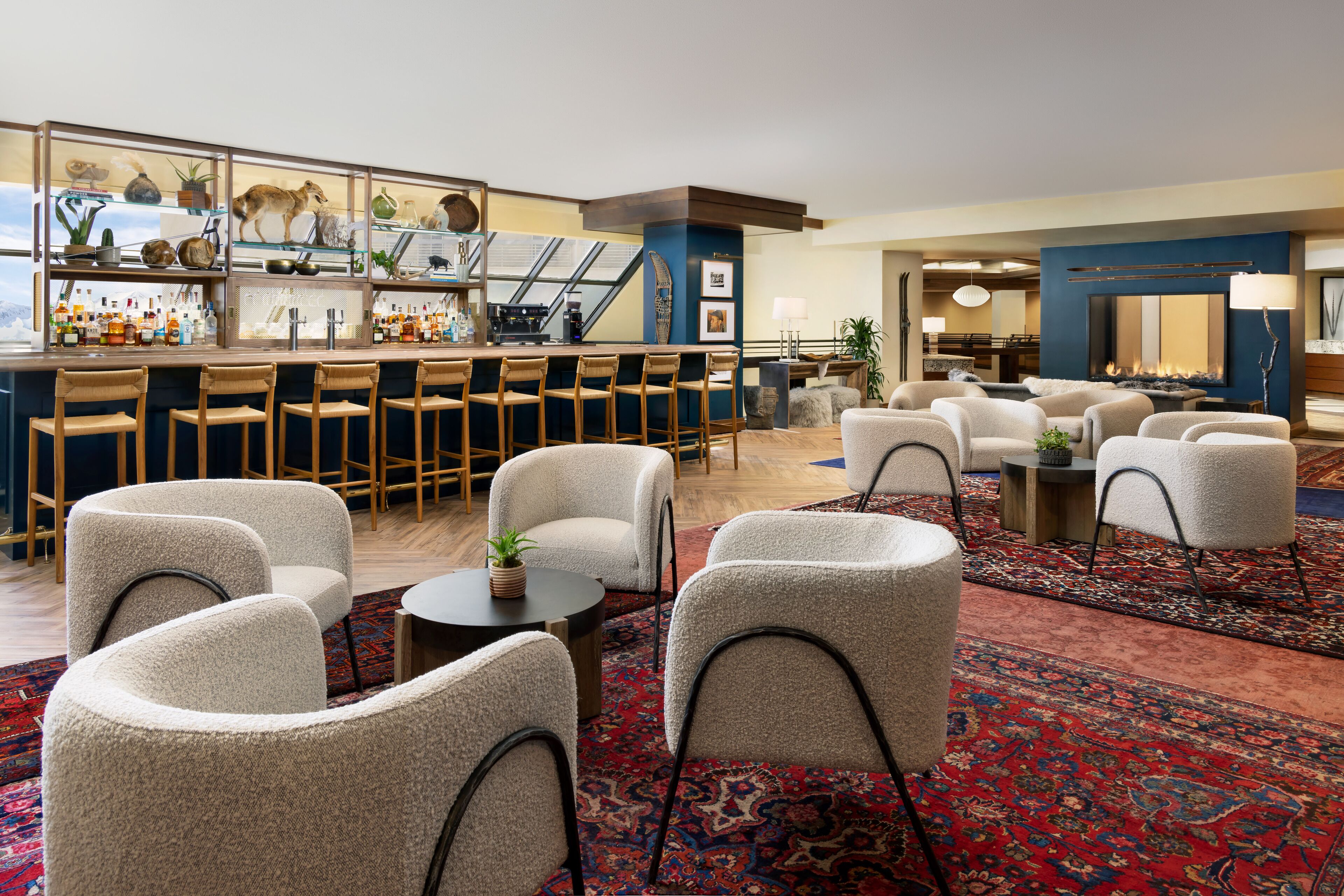 A bar area with stools and a bar counter, a seating area with chairs and a table, and a fireplace in the background.