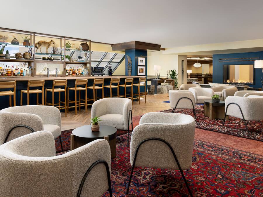 A bar area with stools and a bar counter, a seating area with chairs and a table, and a fireplace in the background.
