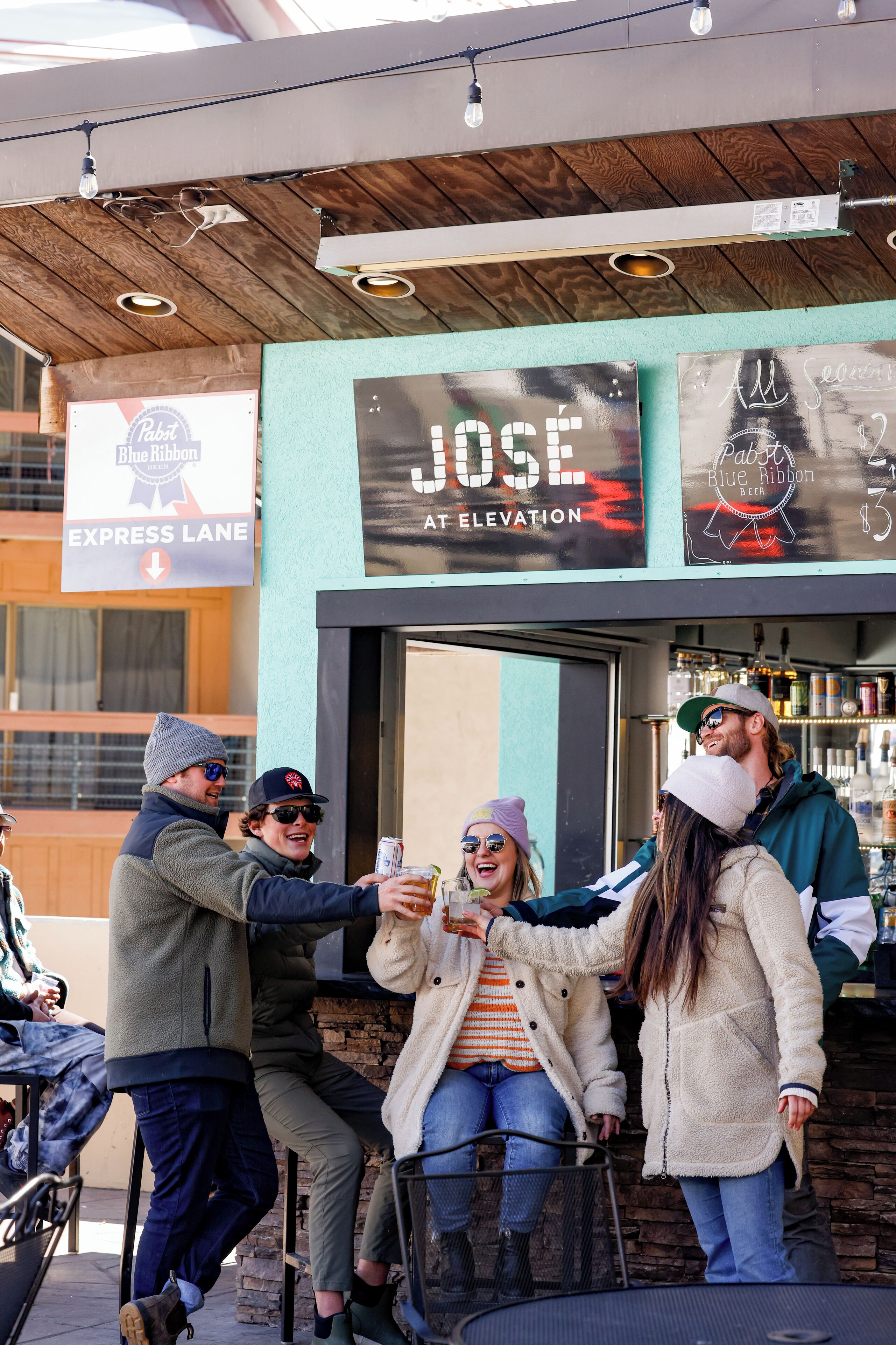 Eine Gruppe von Personen vor einer Bar namens "Jose at Elevation" mit einem Schild, das "Blue Ribbon Beer" bewirbt.