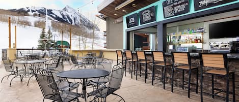 An outdoor cafe with tables and chairs, a bar area, and a menu board.