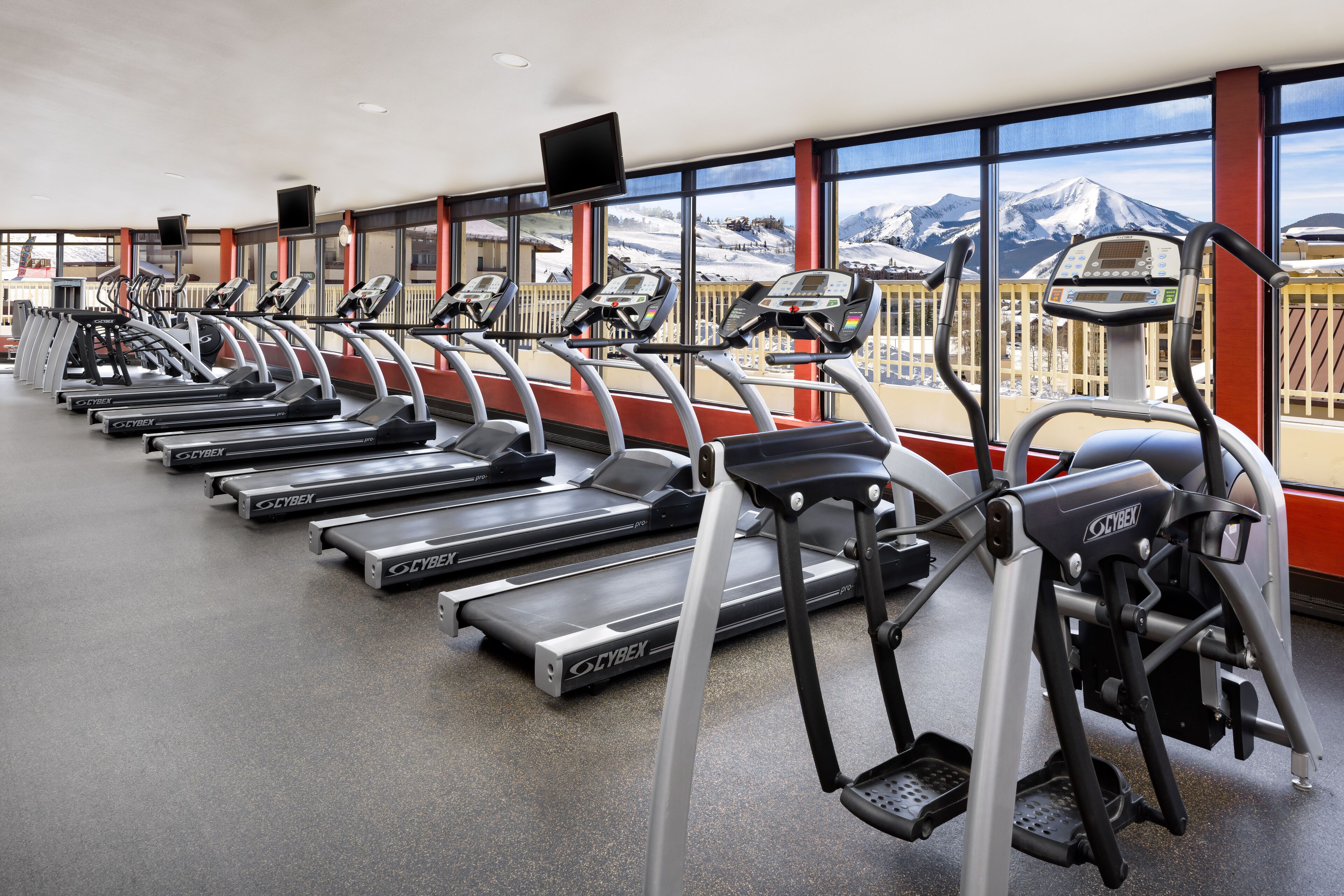 A row of treadmills in a gym with large windows offering a view of snow-capped mountains.
