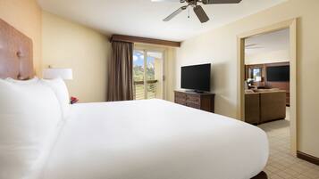 A hotel room with a large bed, a ceiling fan, a television, and a view of the outdoors.