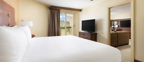 A hotel room with a large bed, a ceiling fan, a television, and a view of the outdoors.
