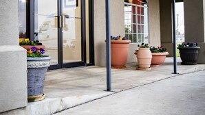 A building entrance with a covered patio, large potted plants, and a glass door. - Days Inn by Wyndham Wagoner (Wagoner)