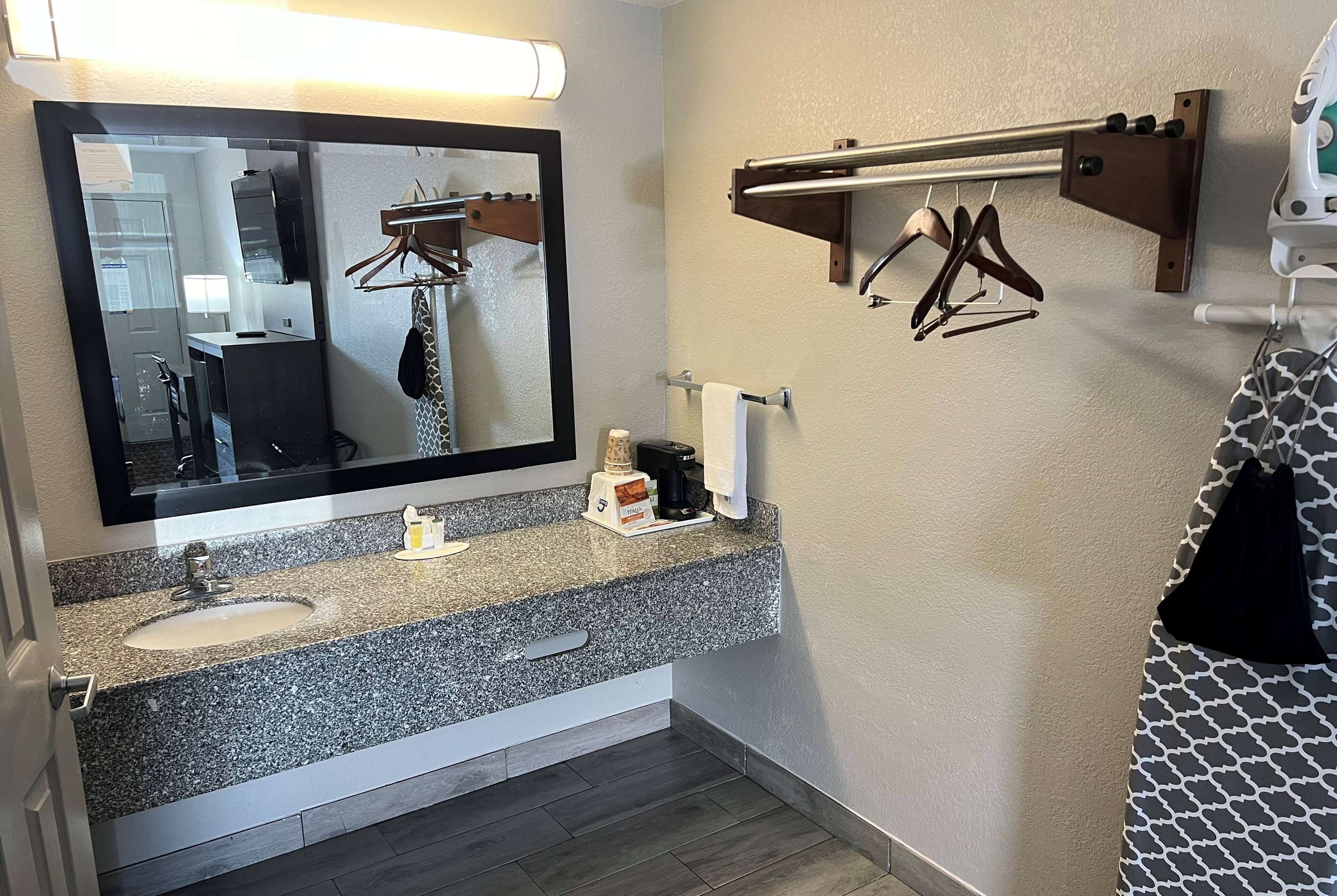 A bathroom with a granite countertop sink, a mirror, a towel rack, and a towel dispenser.