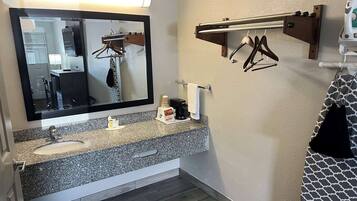 A bathroom with a granite countertop sink, a mirror, a towel rack, and a towel dispenser.
