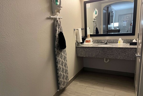 A bathroom with a granite countertop, a mirror, a towel rack, and a shower area.