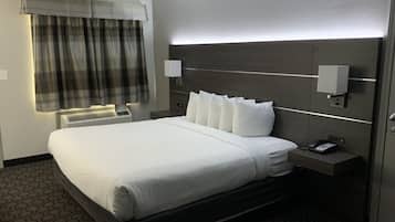 A hotel room with a large bed, a bedside telephone, a nightstand, a wall-mounted lamp, and a window with curtains.
