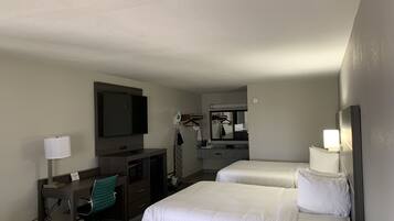 A hotel room with two beds, a desk with a chair, a television, a mirror, and a small kitchenette.