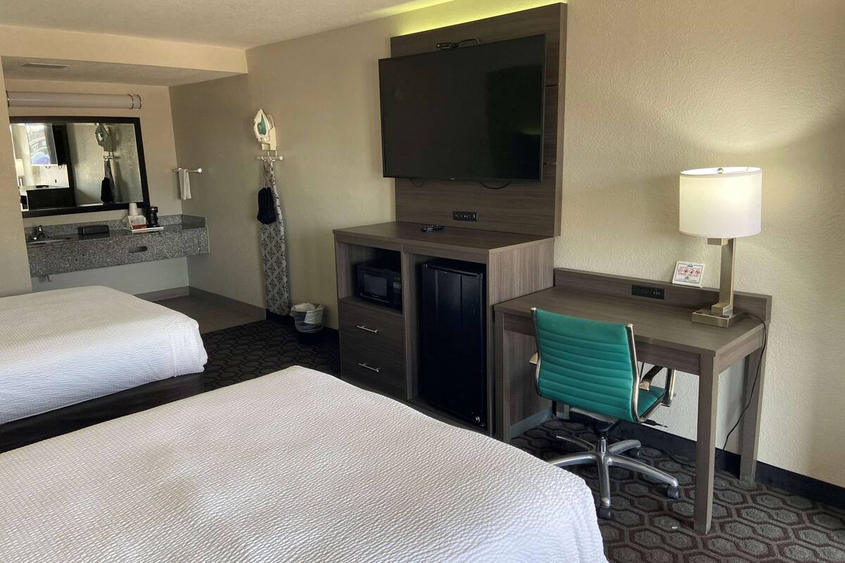 A hotel room with two beds, a desk, a television, and a lamp.