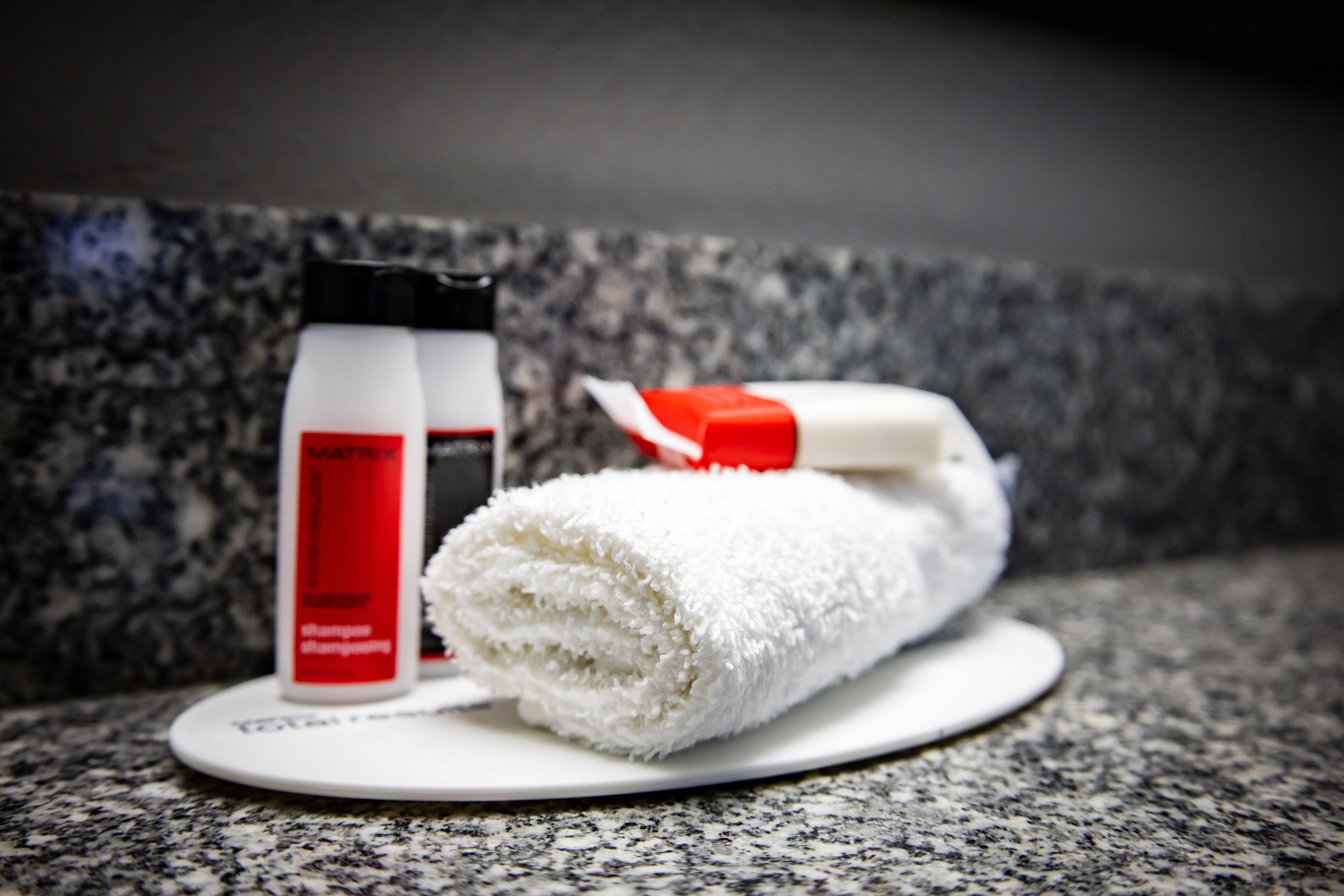 A bathroom counter with a white towel, a red and white toothbrush, and a bottle of shampoo.