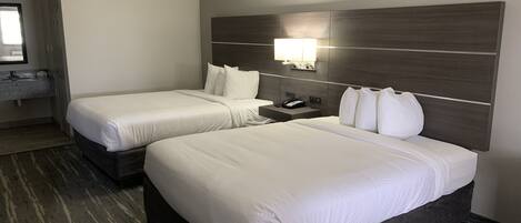 Habitación de hotel con dos camas, una mesita de noche, una lámpara y un baño visible a través de una puerta abierta.