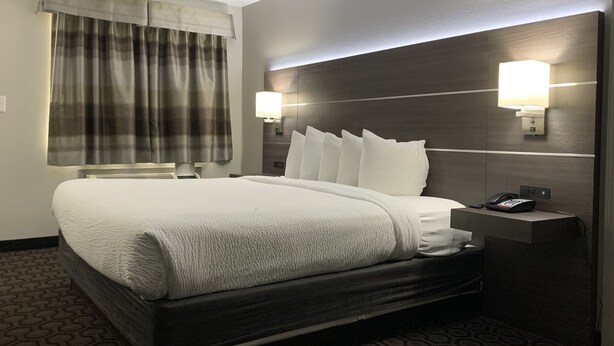 A hotel room with a large bed, a bedside table with a phone, and a window with curtains. - Days Inn by Wyndham Wagoner (Wagoner)