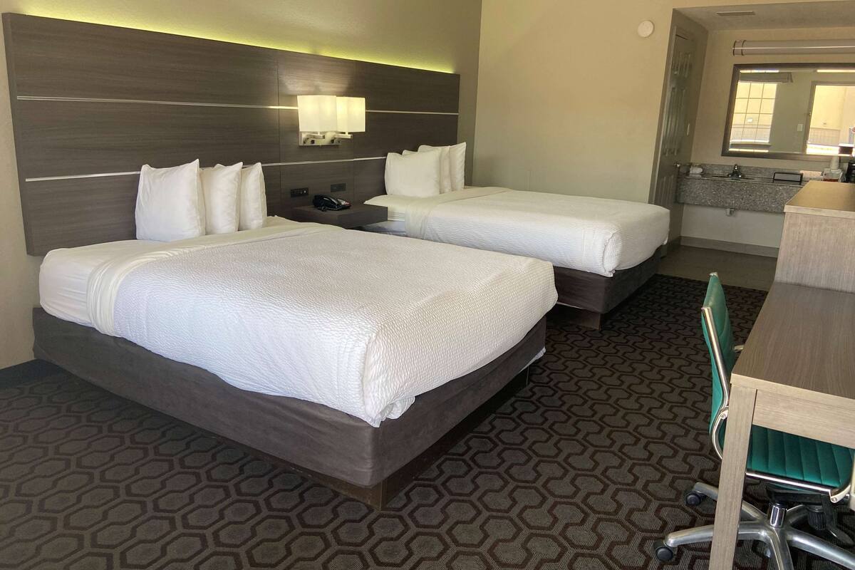 A hotel room with two beds, a desk, a chair, a bathroom, and a patterned carpet.