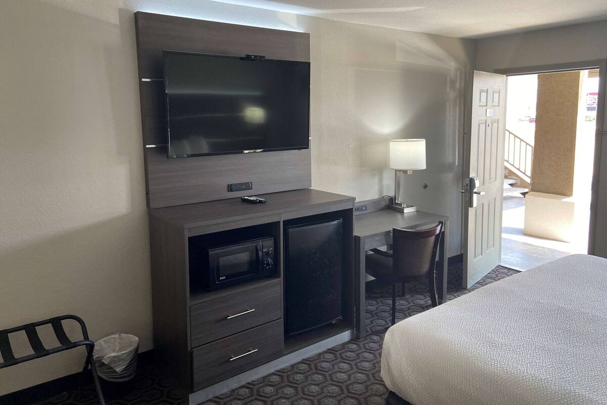 A hotel room with a bed, a desk with a chair, a television, a microwave, and a small refrigerator.
