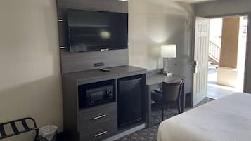 A hotel room with a bed, a desk with a chair, a television, a microwave, and a small refrigerator.