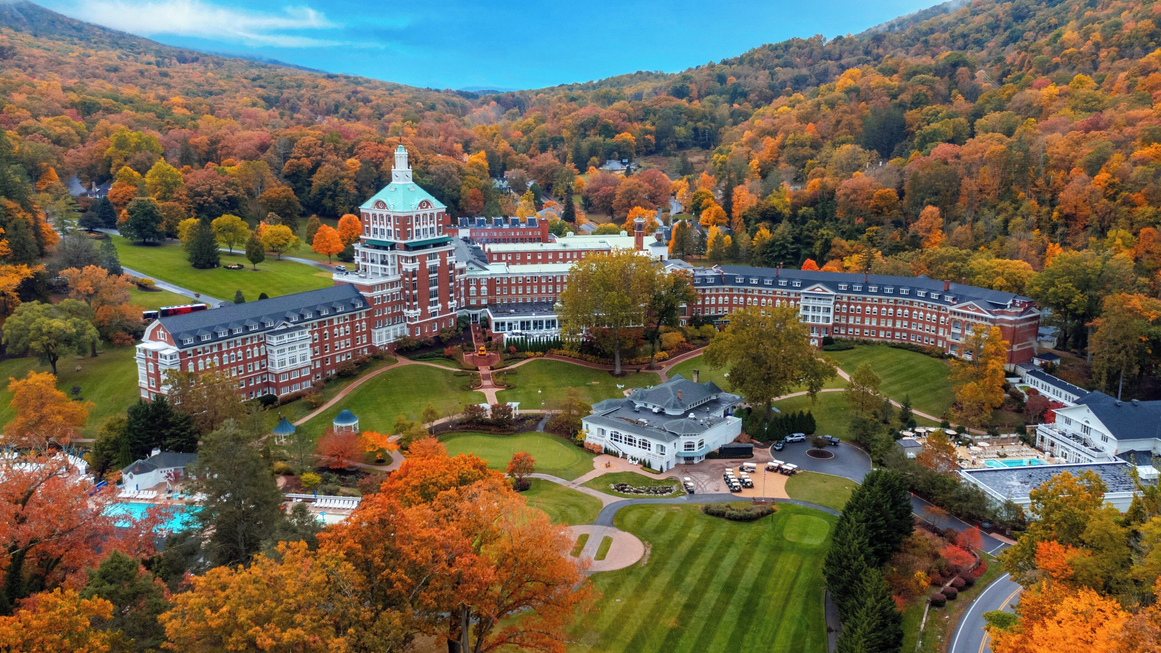 A large, historic building with a central tower, surrounded by manicured lawns and autumn foliage.