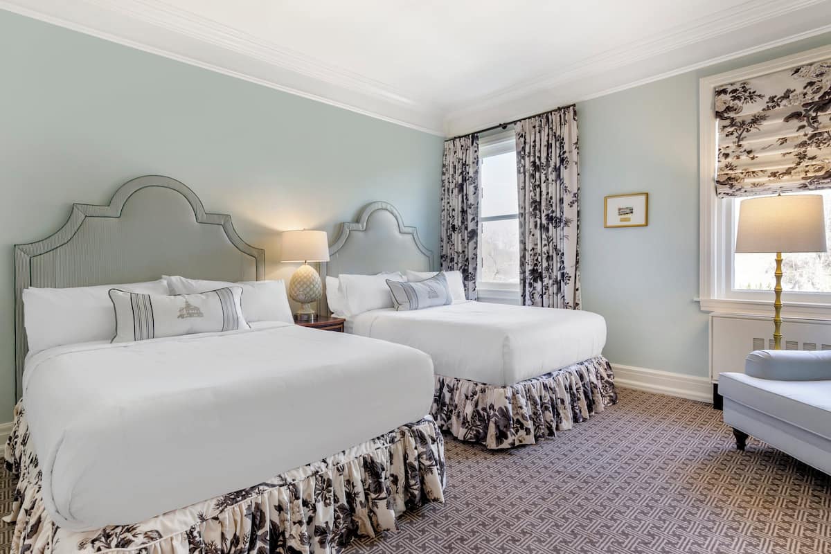 A hotel room with two beds, a small sofa, and a window with floral curtains.
