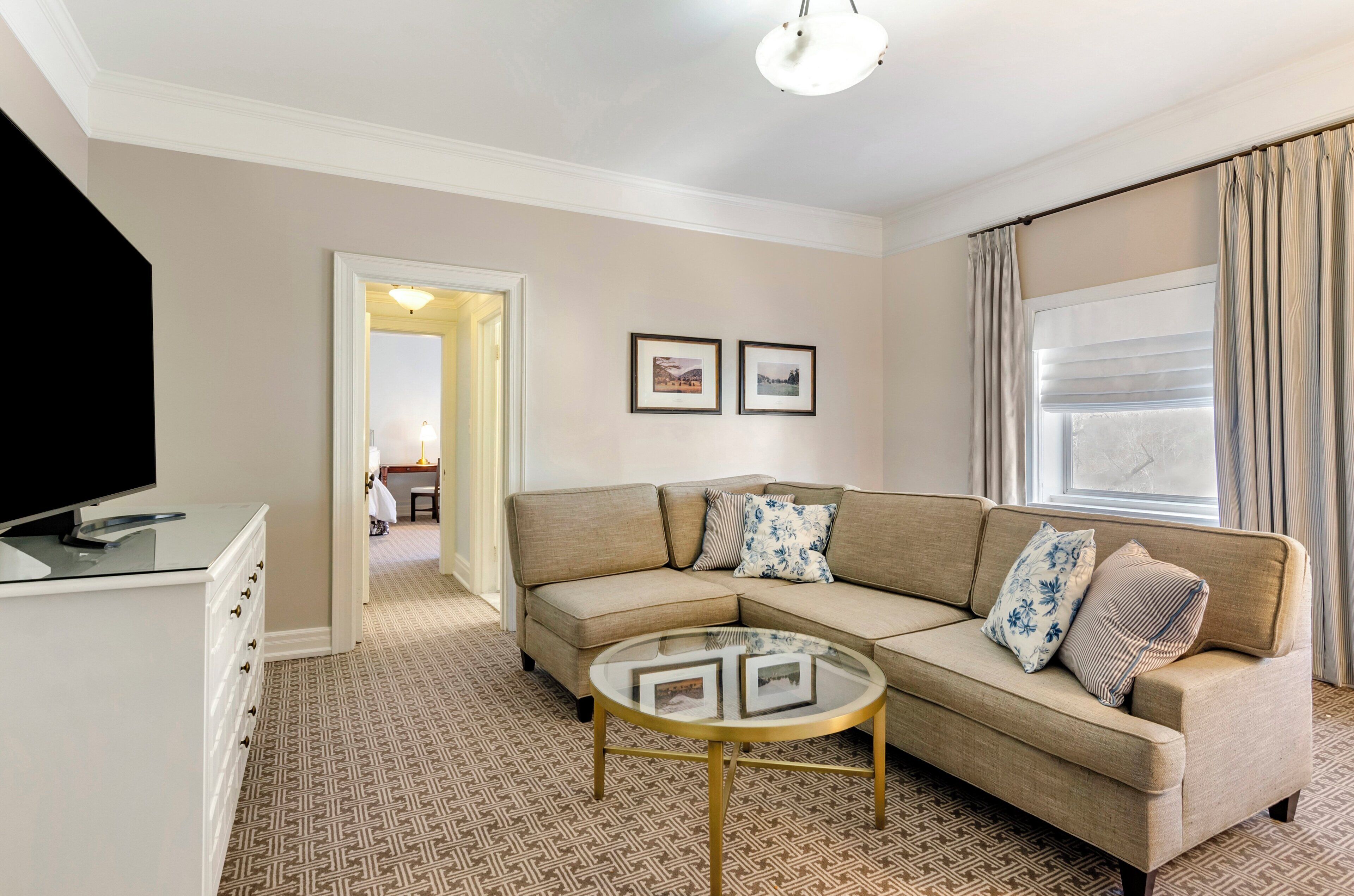 A living room with a beige sofa, a glass coffee table, and a television on a stand.