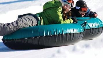 Two people sledding on inflatable tubes in a snowy environment.