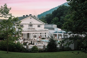 A large white building with a pool and a staircase leading to a balcony.