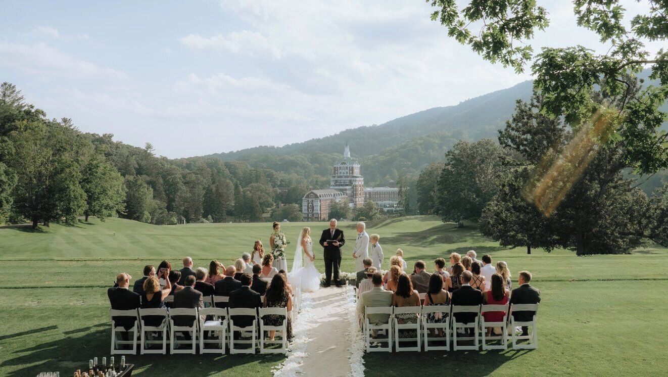 A wedding ceremony on a golf course with a large building in the background.