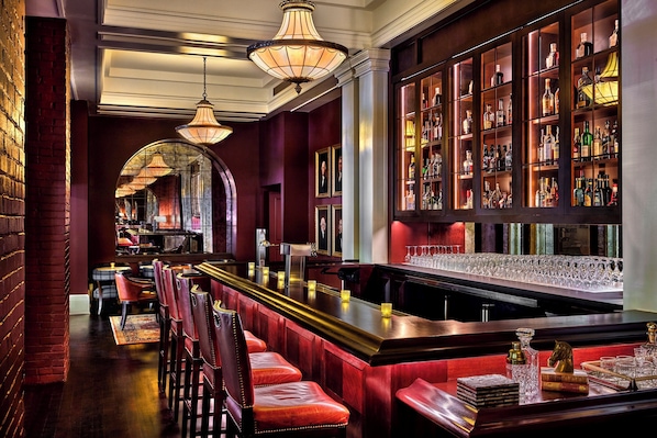 A bar area with a long counter, cushioned seating, and a wine rack.