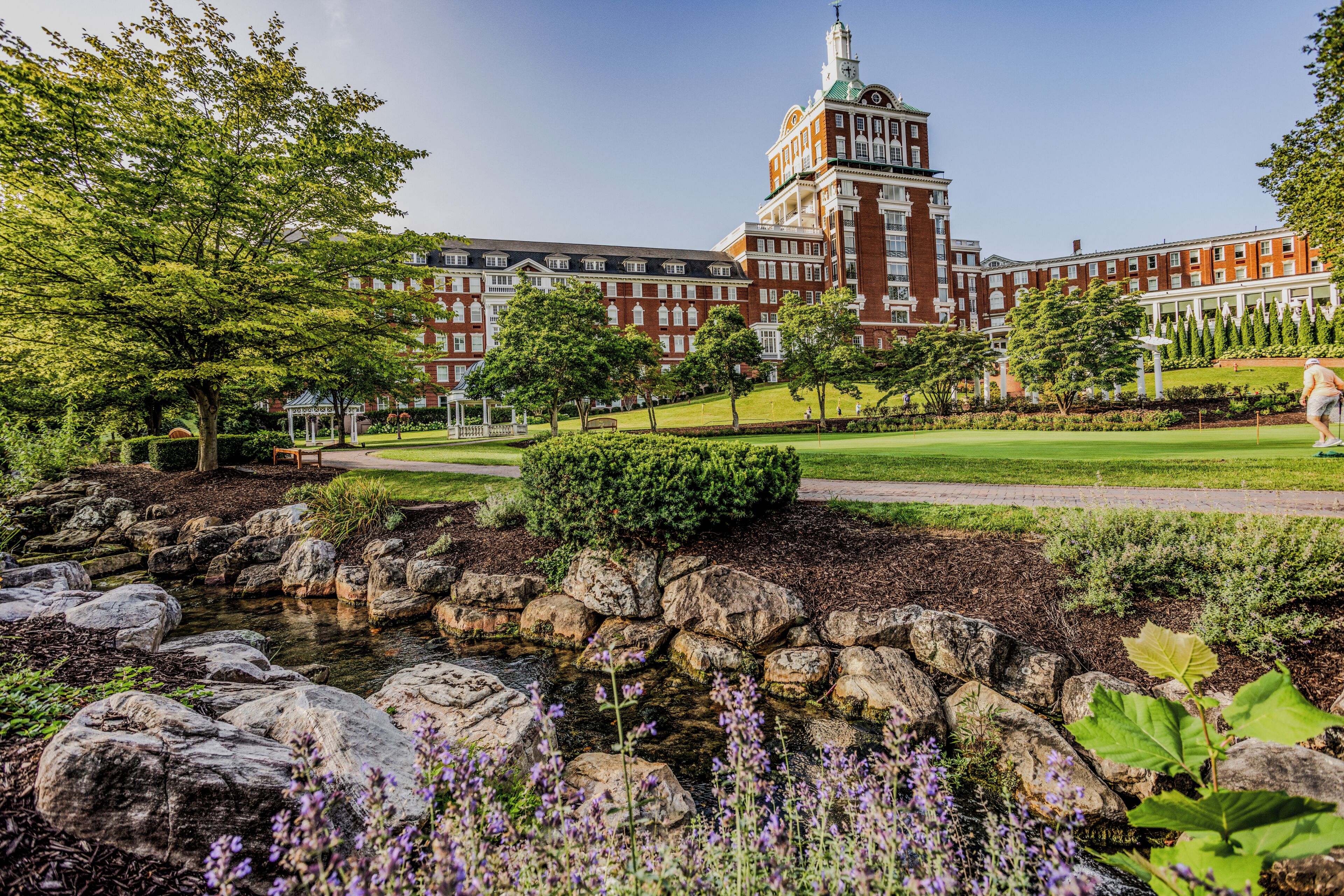 A large building with a prominent tower and a well-maintained garden with a pond and rocks.