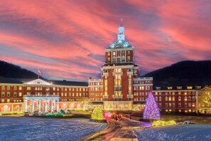 A large building with a prominent clock tower, surrounded by snow-covered ground and decorated with Christmas trees and lights. - The Omni Homestead Resort & Spa (Hot Springs)