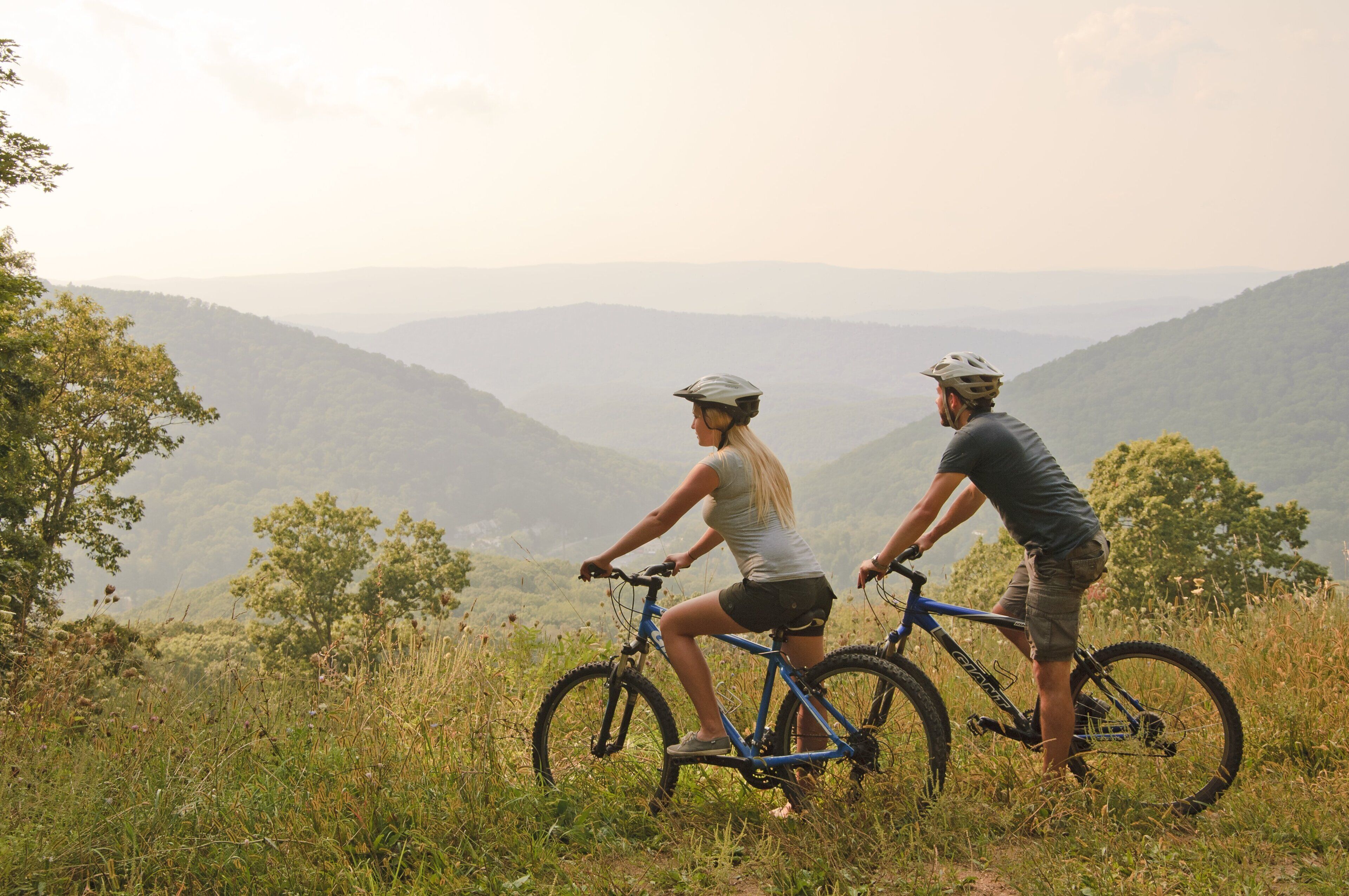 Two people on bicycles on a grassy hill with a view of distant mountains.