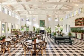 A spacious indoor area with high ceilings, large windows, and numerous tables and chairs.