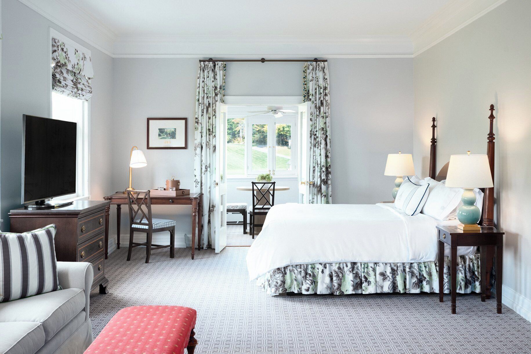 A hotel room with a bed, desk, chair, television, and a view of the outdoors.