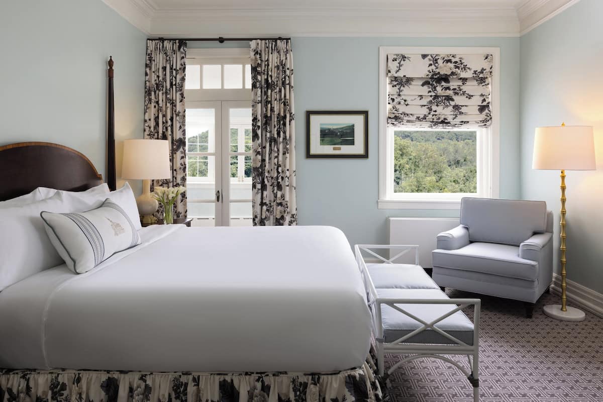 A neatly arranged bedroom with a large bed, a chair, a lamp, and a window with curtains.