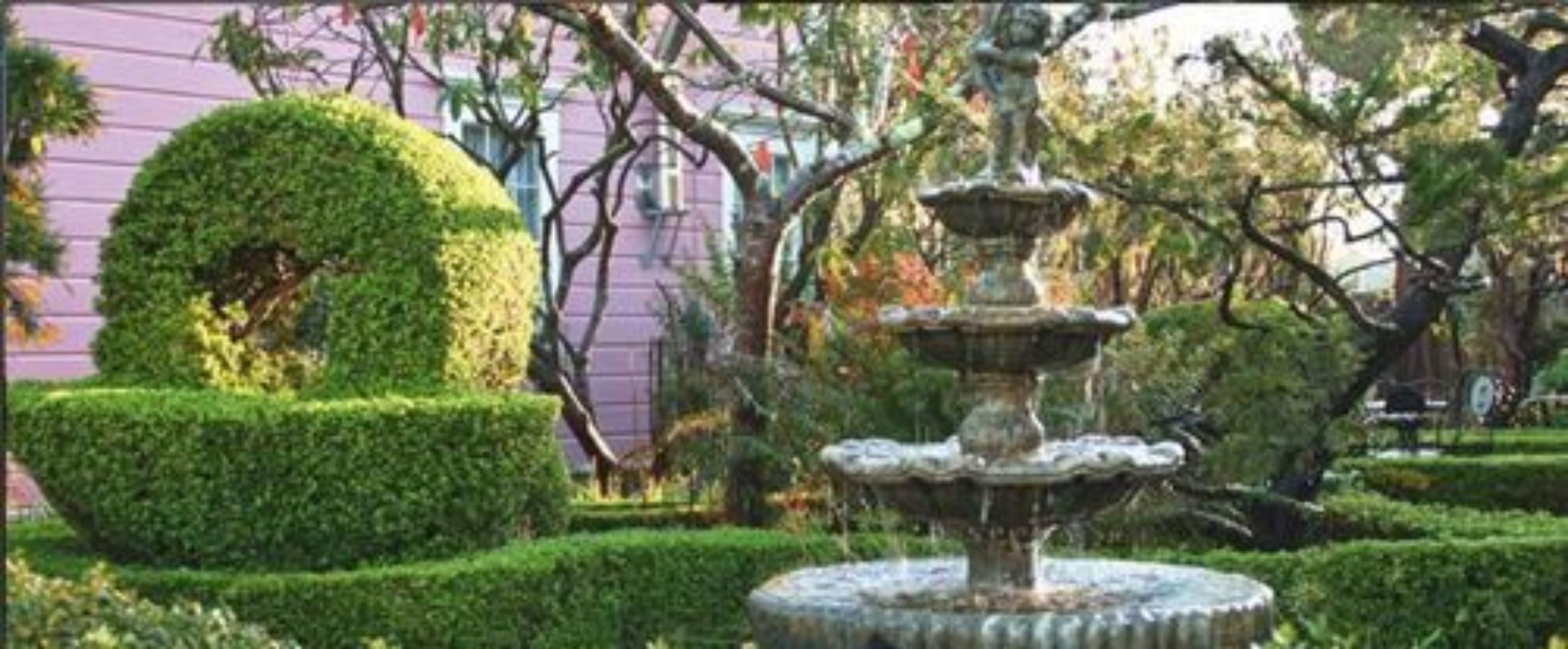 Un jardín con una fuente de piedra escalonada, rodeada de setos y árboles bien cuidados.
