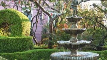 Un jardín con una fuente de piedra escalonada, rodeada de setos y árboles bien cuidados.