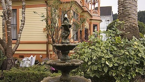 A multi-story building with a corner turret and a fountain in the foreground. - Gingerbread Mansion Inn (Ferndale)