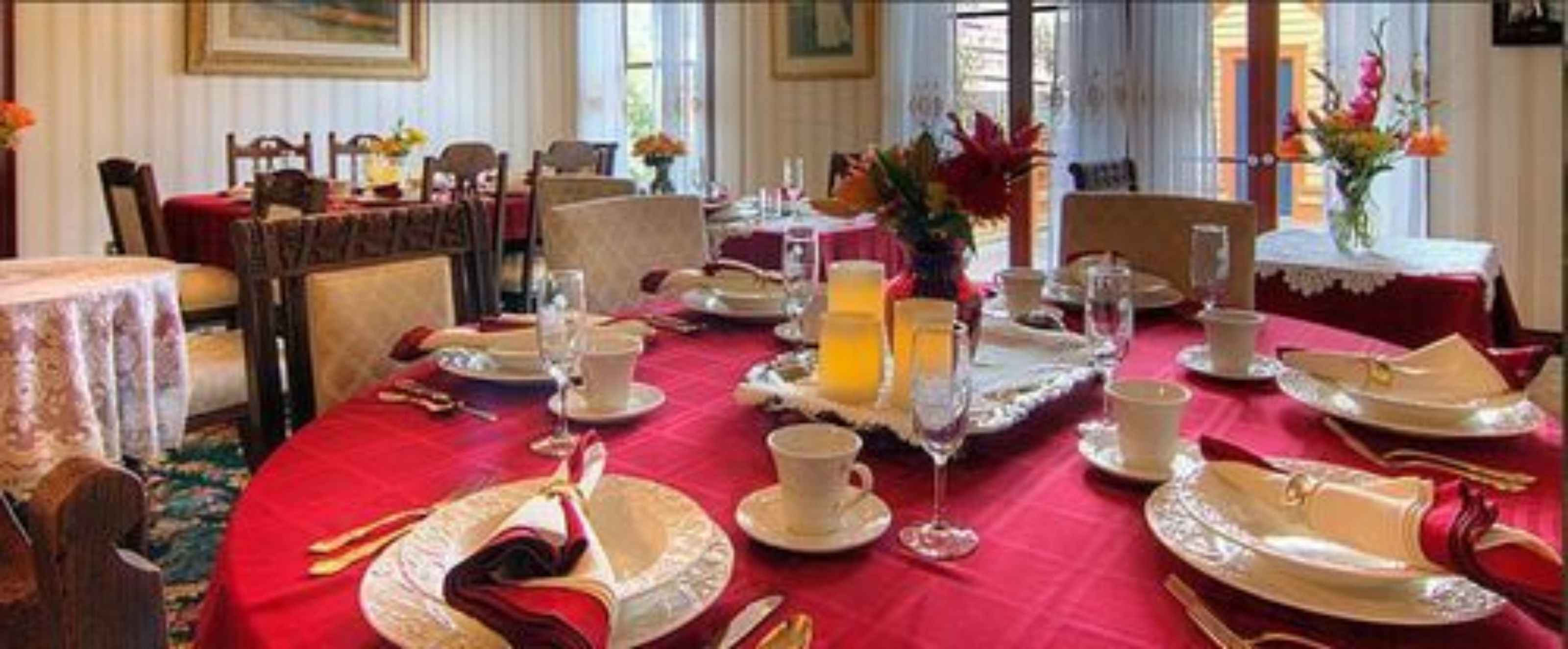 A dining area with red tablecloths, white plates, and silverware. There are floral centerpieces on the tables.
