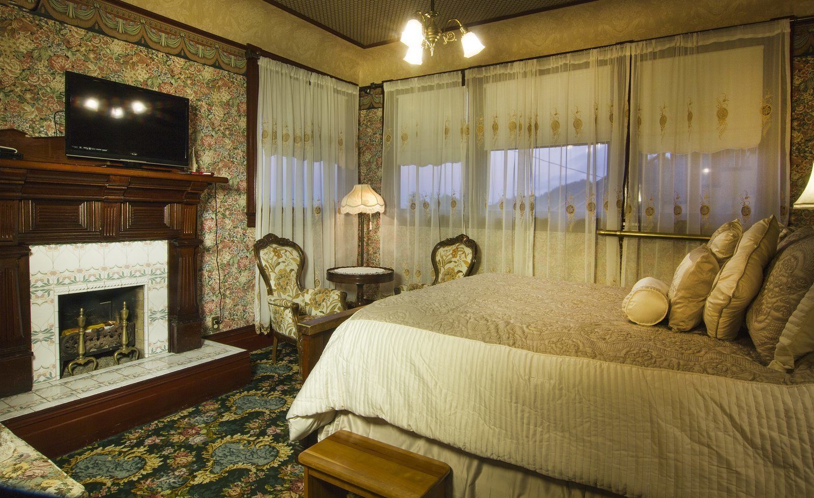 A traditional room with a fireplace, a bed with multiple pillows, a chair, a small table, and a television.