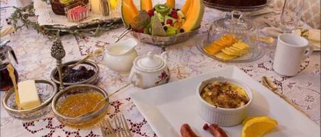 A table set with various breakfast items including a fruit bowl, a cake, and a plate with sausages and lemon slices.