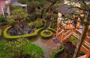 A courtyard with a circular hedge, a small fountain, and a staircase leading to an upper level.
