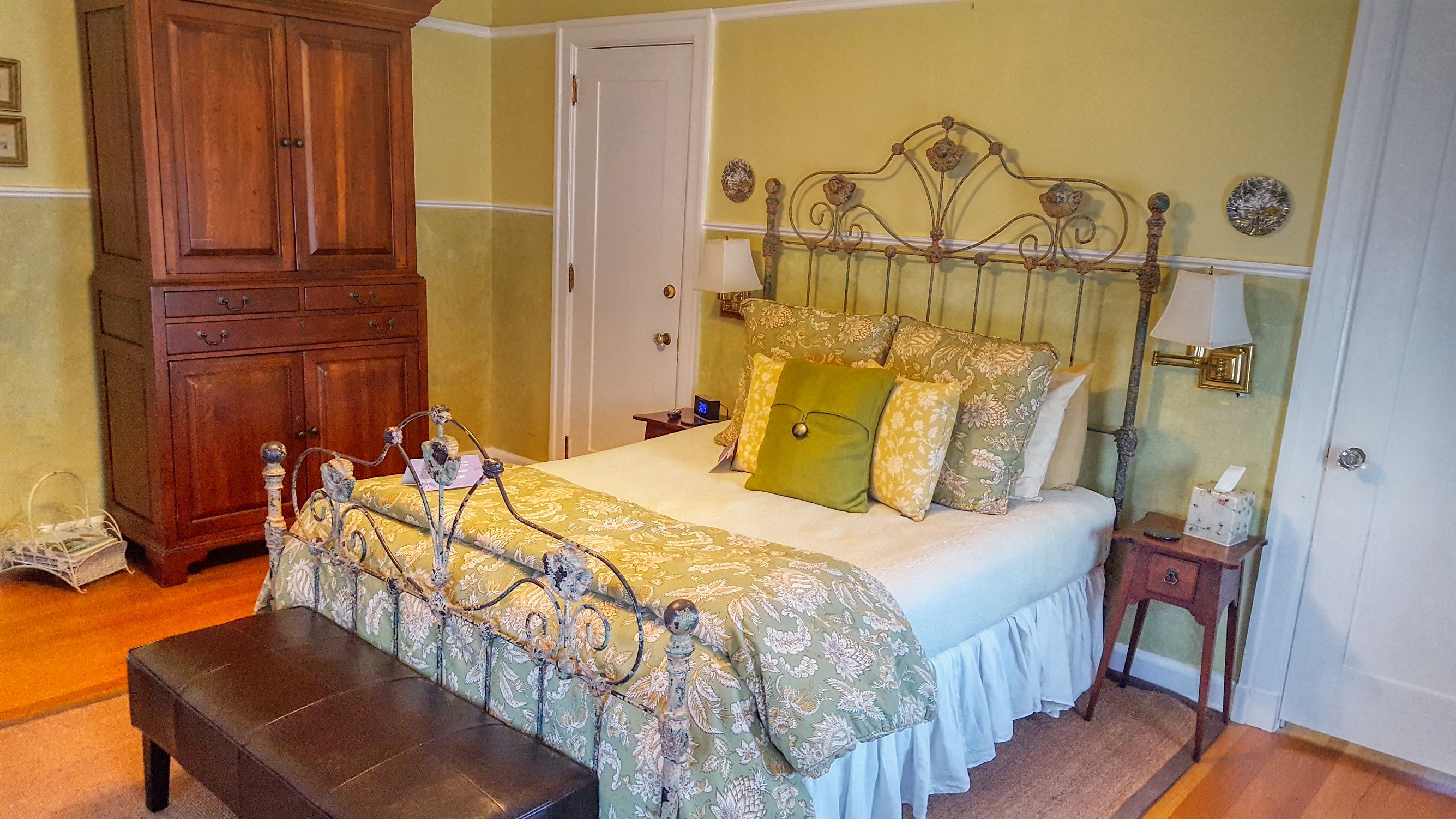 A bedroom with a large bed, a wooden wardrobe, a bedside table with a lamp, and a bench.