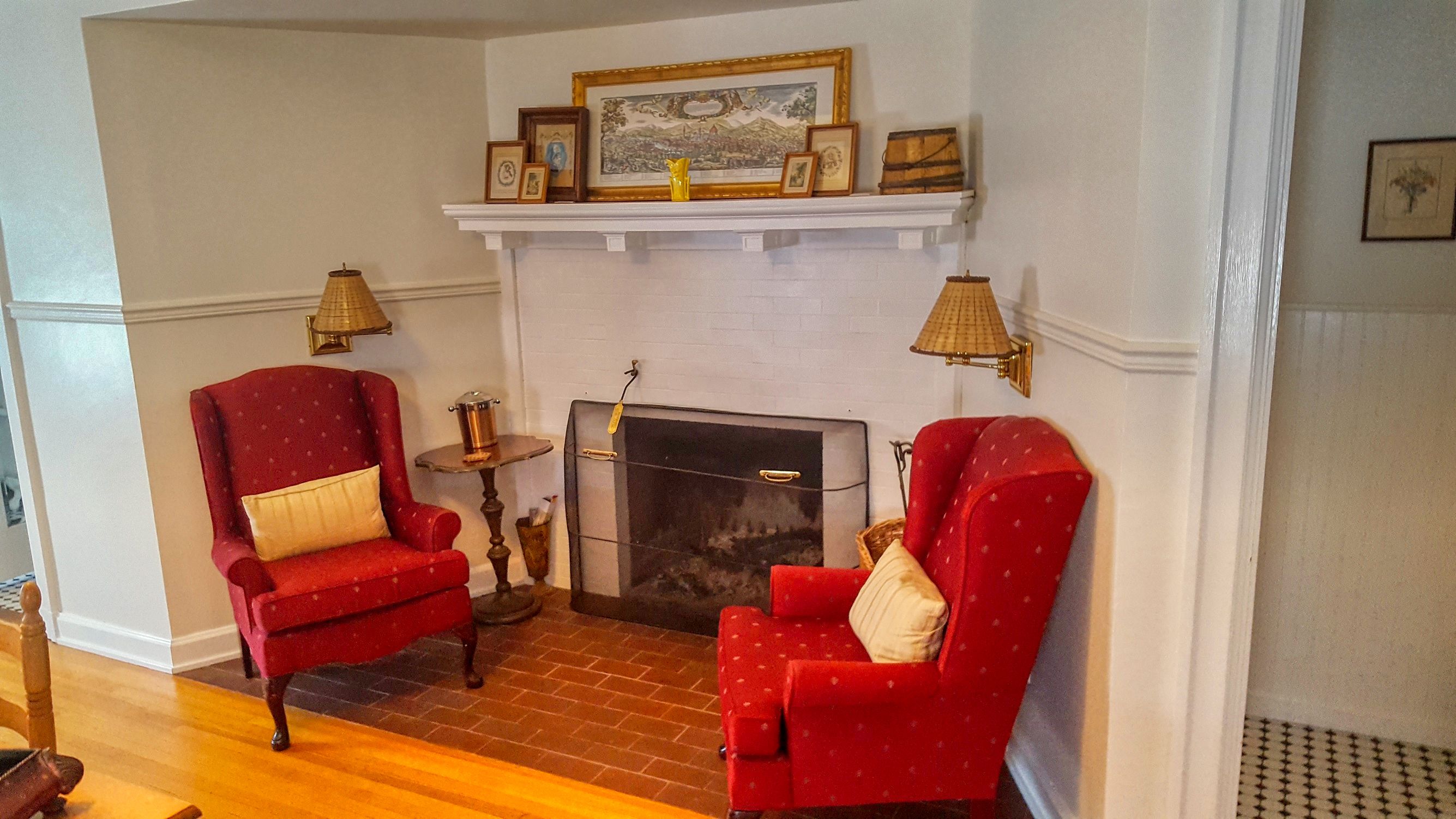 A room with a fireplace, two armchairs, a small table, and wall-mounted lamps.