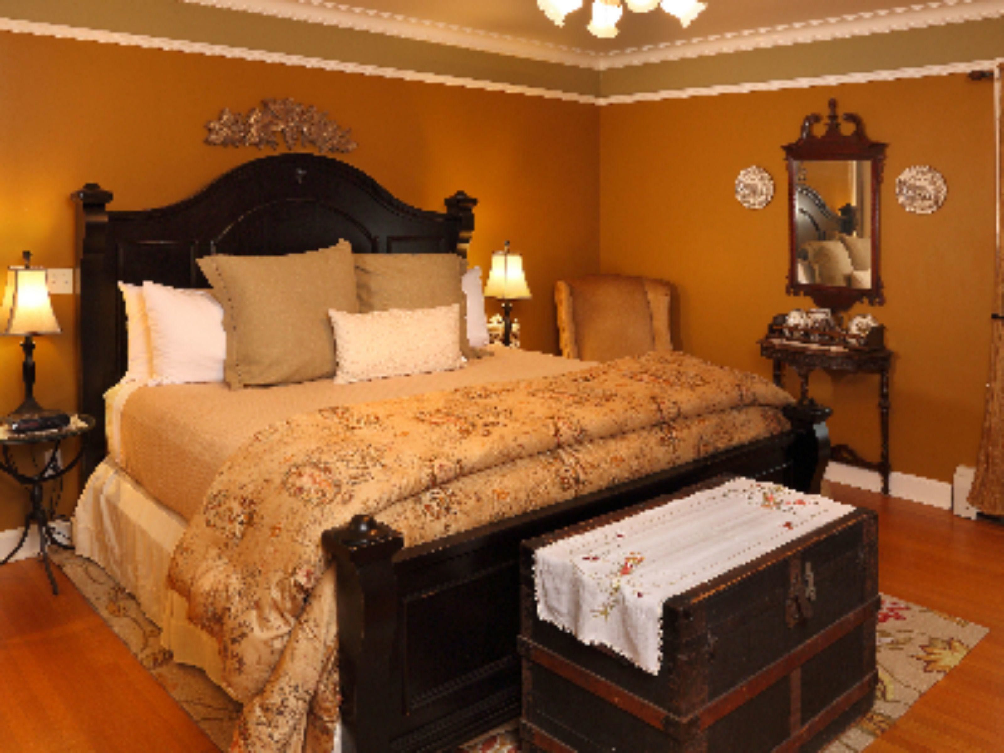 A bedroom with a large bed, two bedside tables with lamps, a chair, a dresser, and a mirror on the wall.