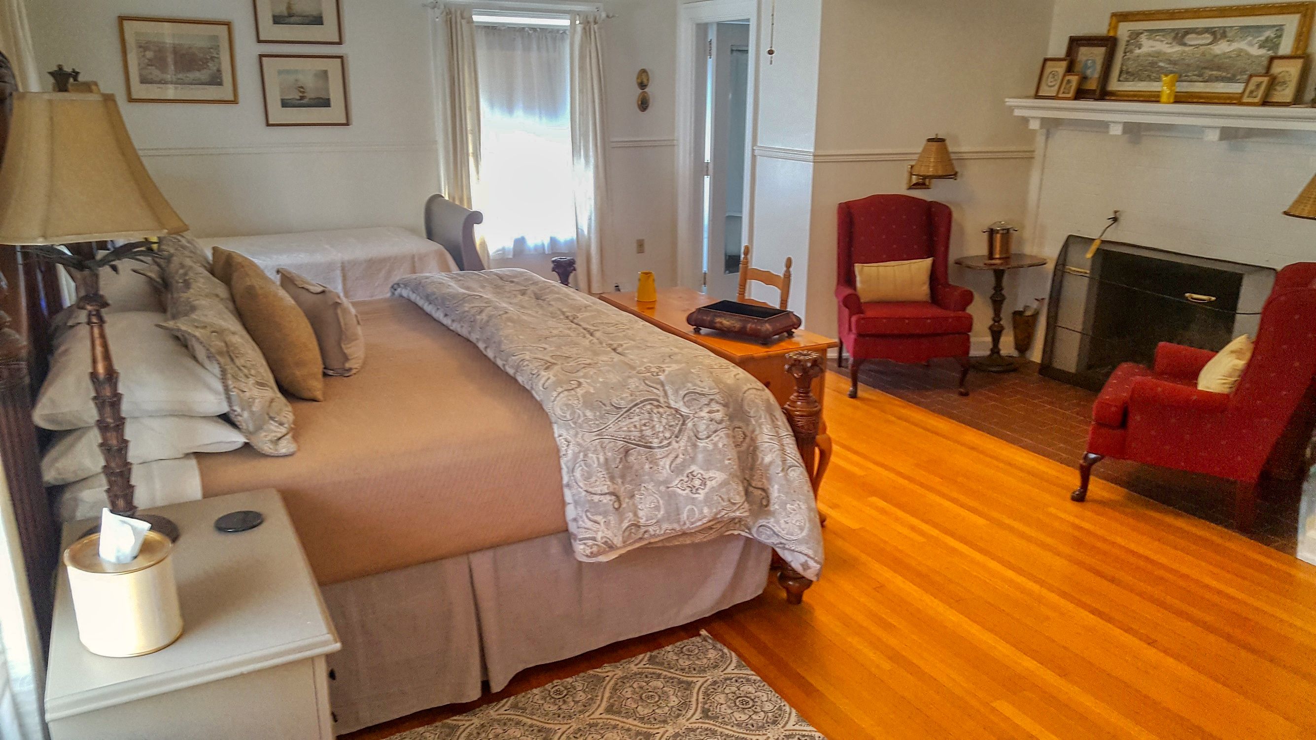 Un dormitorio con cama, una silla, una lámpara, chimenea y alfombra.