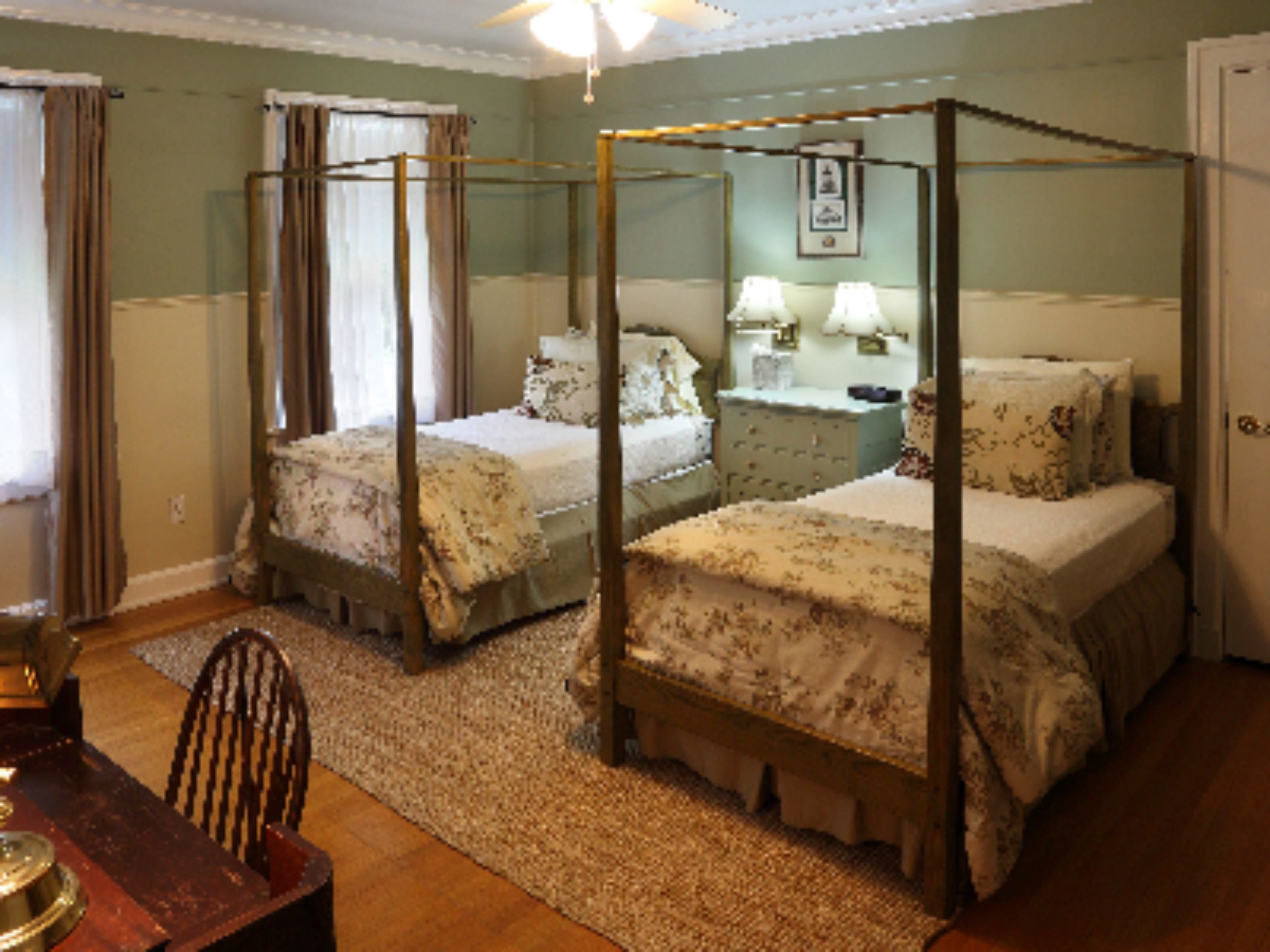 A bedroom with two four-poster beds, a wooden chair, a nightstand, and a dresser.