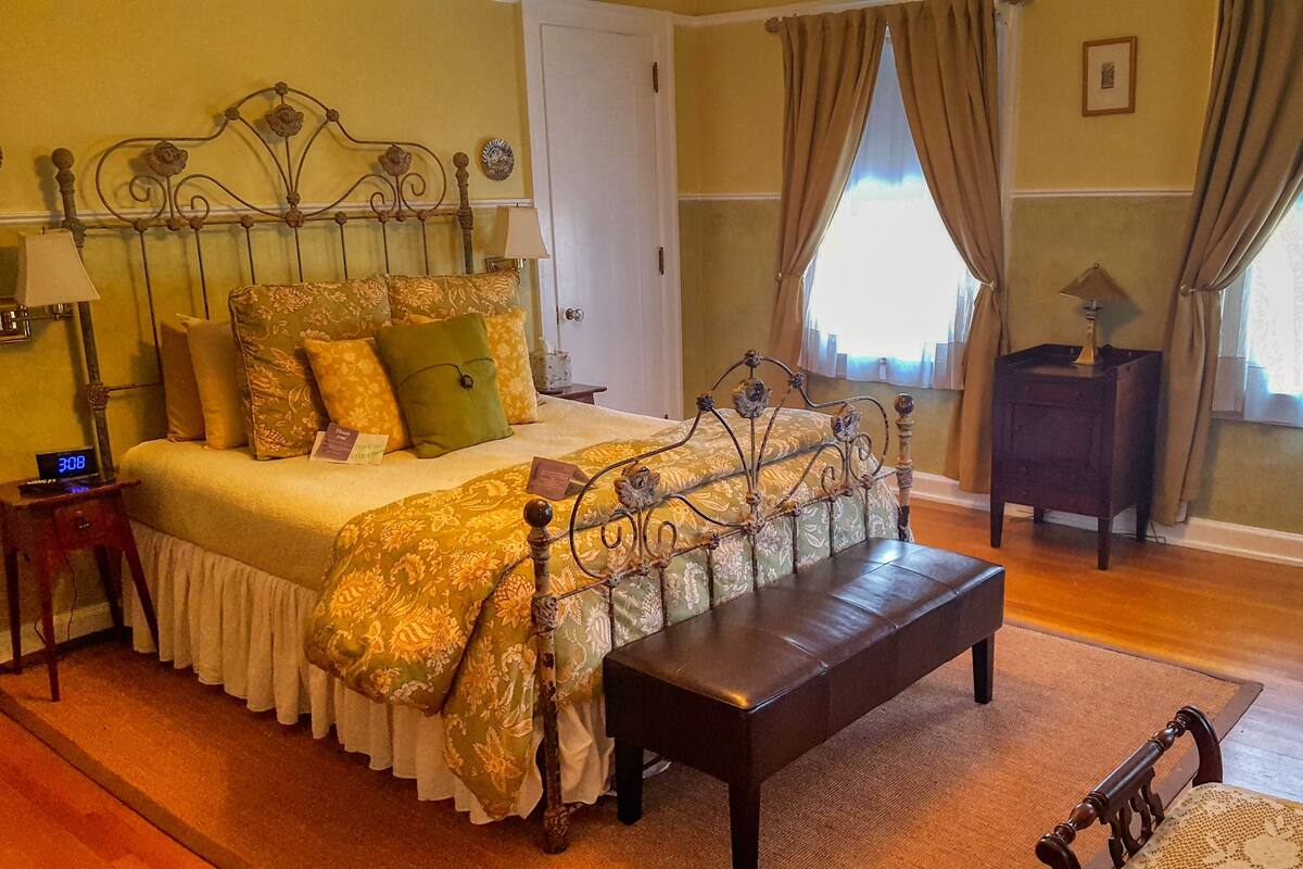 A neatly arranged bedroom with a bed, bedside table, lamp, bench, and a chair.